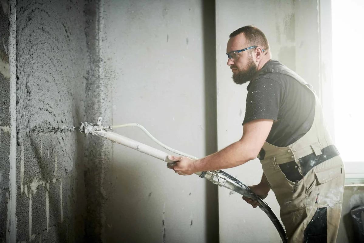 Radnik mašinski nanosi malter na blok zid pomoću creva sa mlaznicom